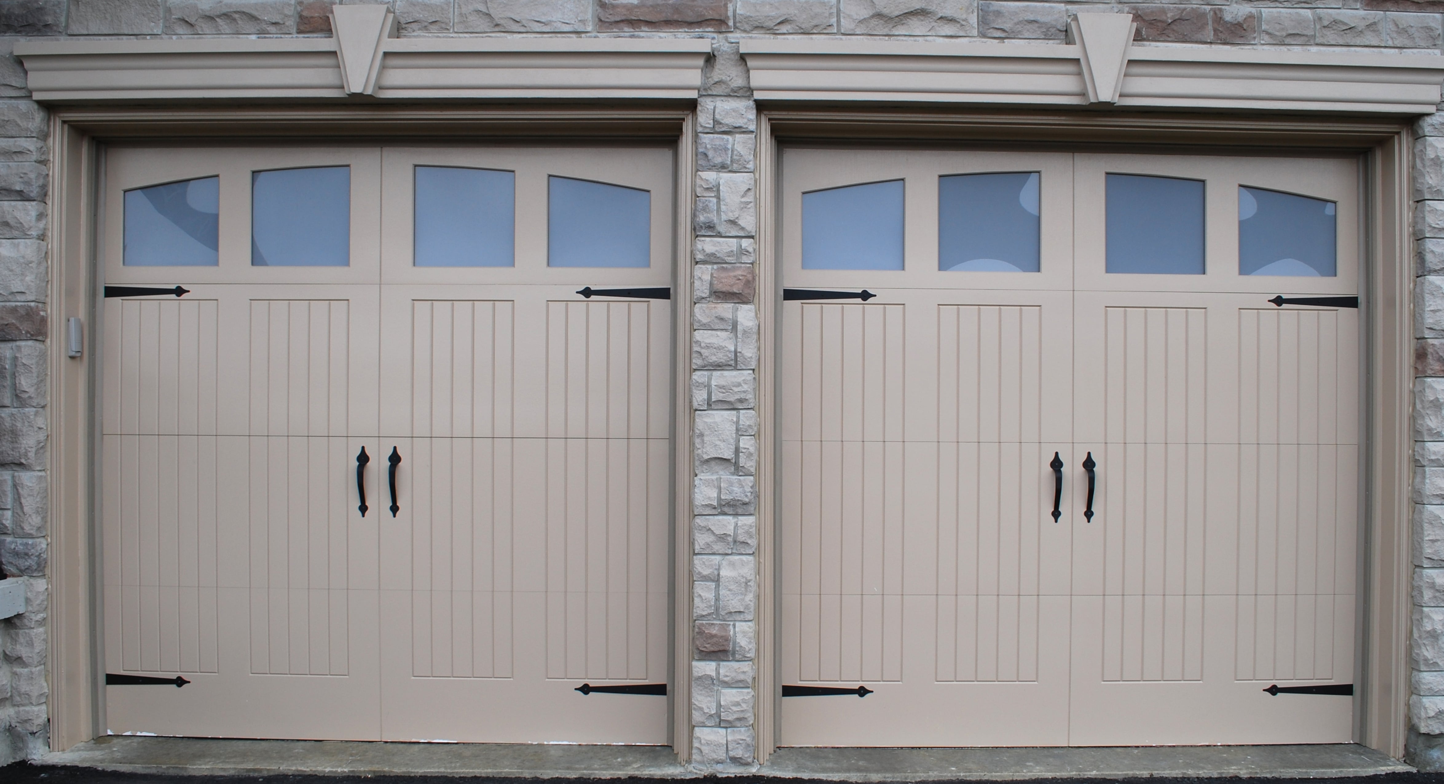Beautiful custom garage doors with windows and decorative hardware professionally installed on stone home